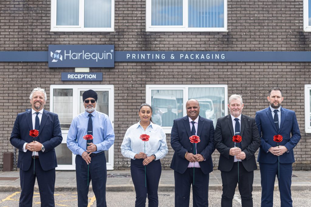 Colleagues in business attire hold metal red roses outside their office.